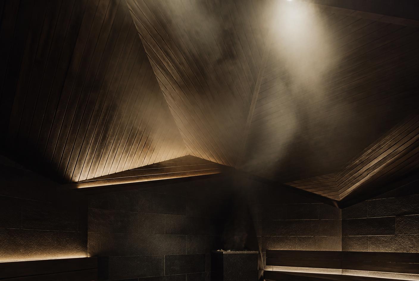 Steam gathering against a sculpted timber ceiling in a dark thermal room